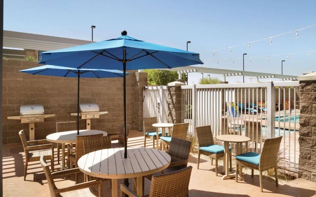 a patio with tables and chairs and a blue umbrella at Home2 Suites By Hilton Glendale Westgate in Glendale