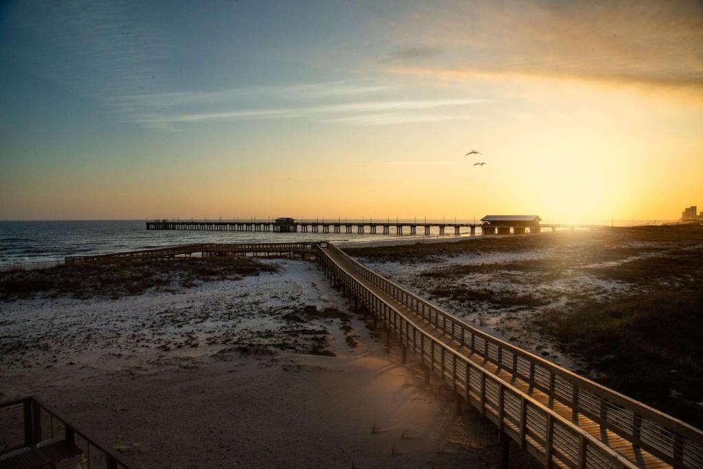 a pier on the beach with the sunset in the background at The Lodge at Gulf State Park, A Hilton Hotel in Gulf Shores
