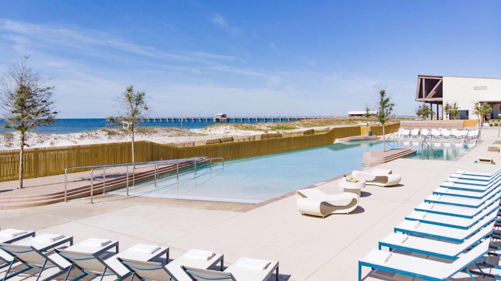a swimming pool with lounge chairs and the beach at The Lodge at Gulf State Park, A Hilton Hotel in Gulf Shores