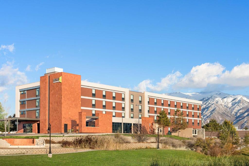 a large brick building with mountains in the background at Home2 Suites by Hilton Salt Lake City/Layton in Layton