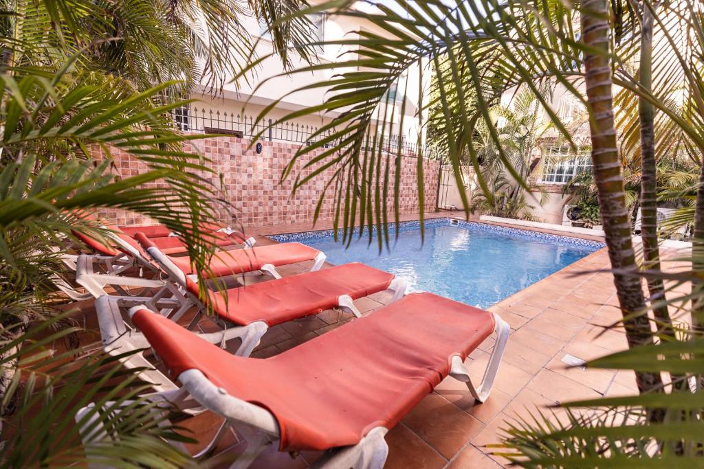 a pool with red lounge chairs next to a swimming pool at Hostal Las Rosas de Punta Cana in Punta Cana