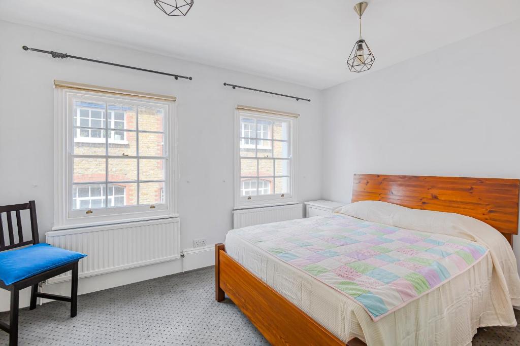 a bedroom with a bed and a chair and two windows at Charming 4 bed town house with roof terrace in London