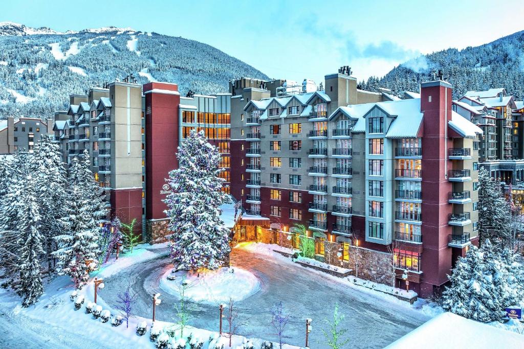 a hotel in the snow with a mountain in the background at Hilton Whistler Resort & Spa in Whistler