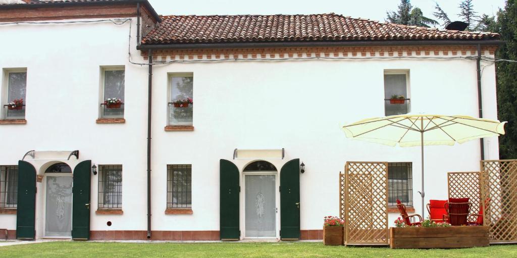 a white house with an umbrella in the yard at B&B Le Stanze del Belriguardo in Voghiera