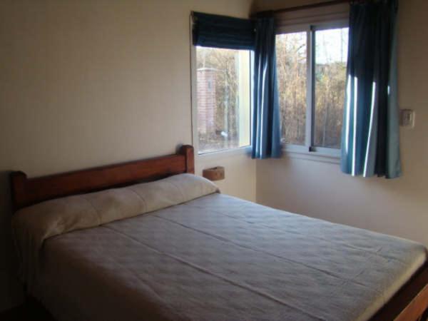 a bedroom with a bed with blue curtains and two windows at Cabañas Mayma in Vaqueros