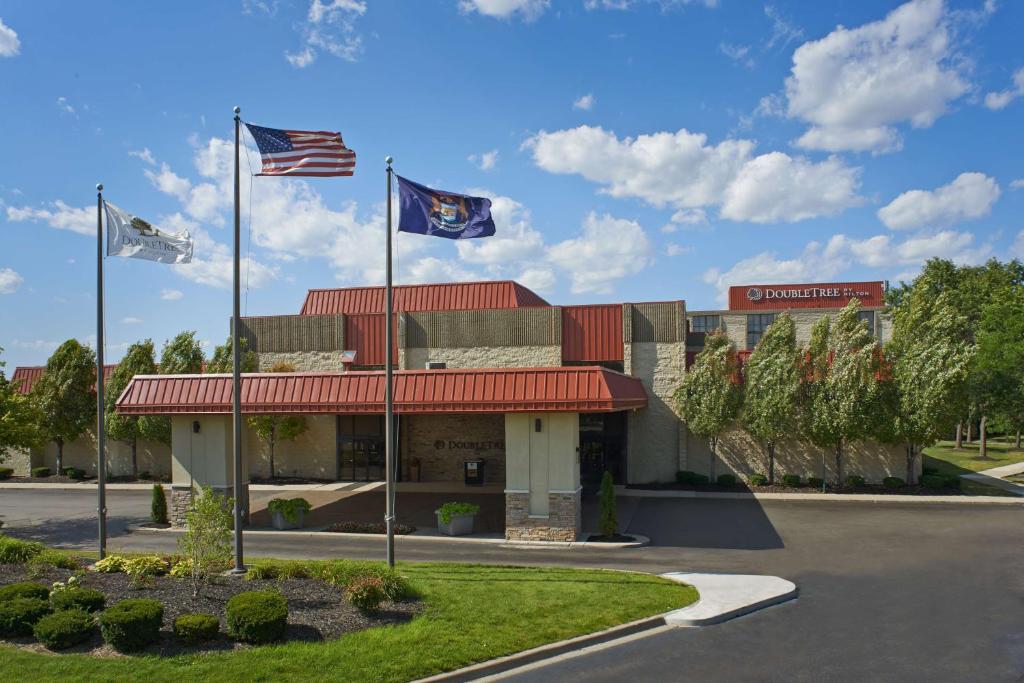 Un hotel con dos banderas frente a un edificio. en DoubleTree by Hilton Dearborn, en Dearborn