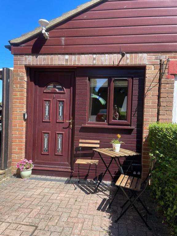 a red house with a table and chairs in front of a door at The Cotswold Nook in Dursley