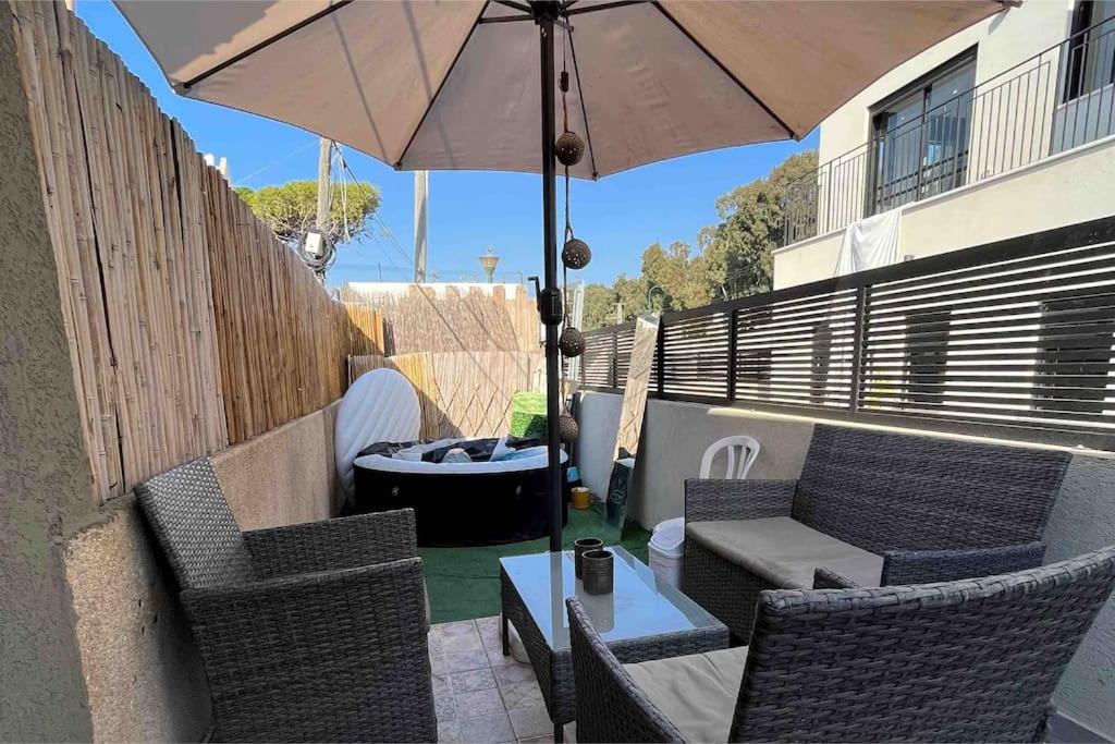 une terrasse avec une table, des chaises et un parasol dans l'établissement דירה נאה ומרווחת עם חצר פרטית, à Netanya