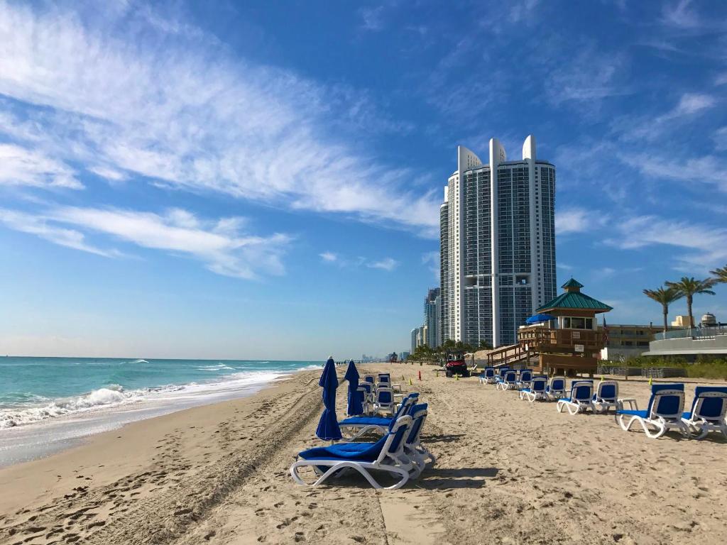 a beach with lounge chairs and a tall building at Sunny Isles Miami HOLIDAY apartment in Miami Beach