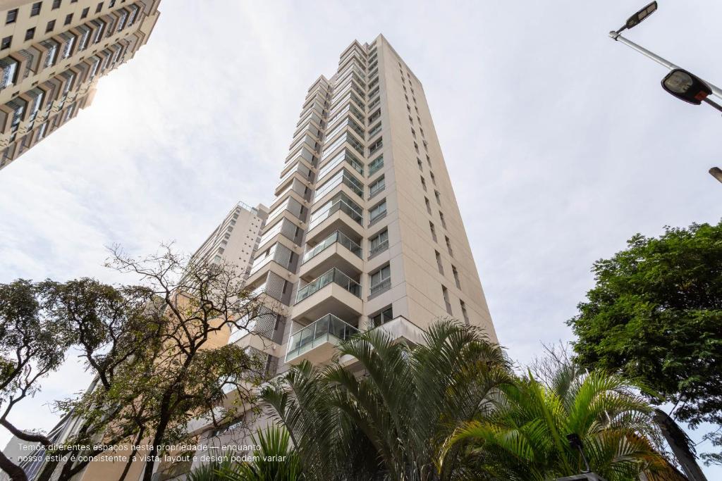 Apartamentos completos em Pinheiros a uma quadra da Faria Lima - HomeLike في ساو باولو: مبنى أبيض طويل وبه أشجار أمامه