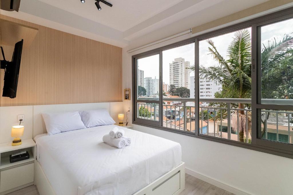um quarto com uma cama branca e uma grande janela em Condomínio ID Lisboa - Studios por temporada em São Paulo