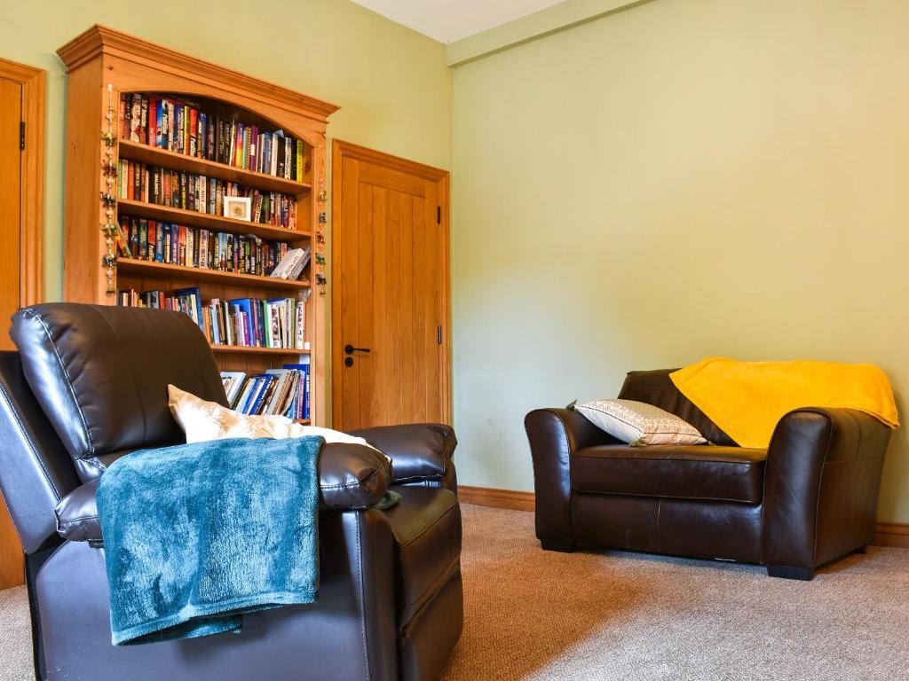 a living room with two chairs and a book shelf at The Old Boot Room in Llanfynydd