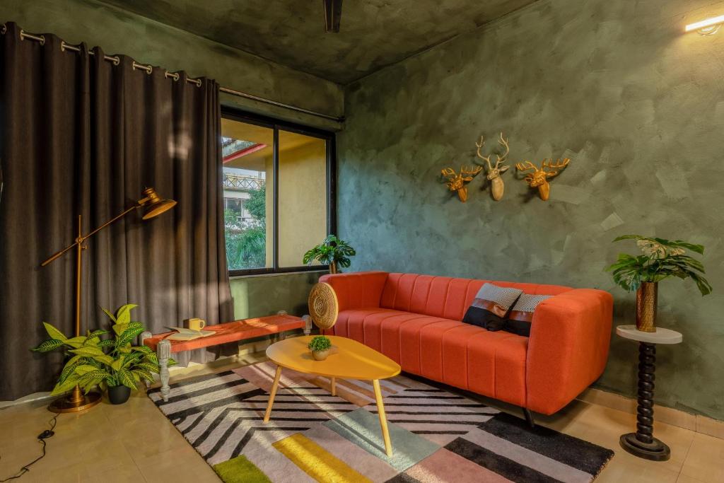 ein Wohnzimmer mit einem roten Sofa und einem Tisch in der Unterkunft Mossy - Aesthetic 2BHK Apartment - Vagator, Goa By StayMonkey in Vagator