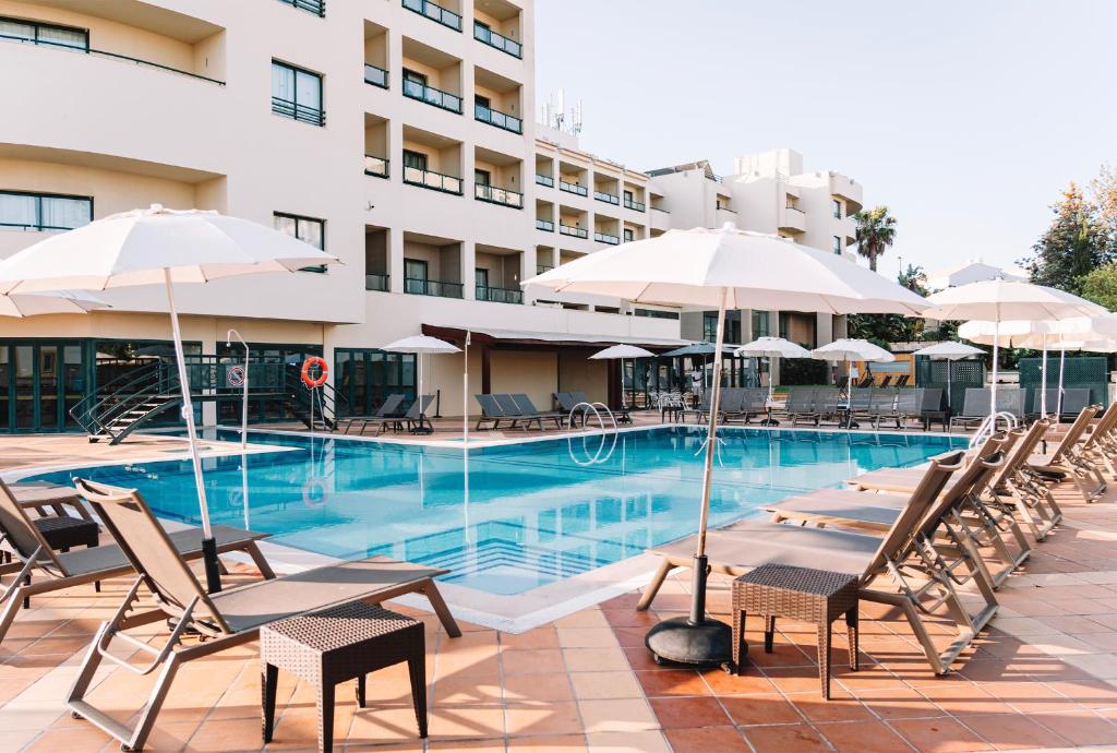 a swimming pool with chairs and umbrellas in front of a building at Real Bellavista Hotel & Spa in Albufeira