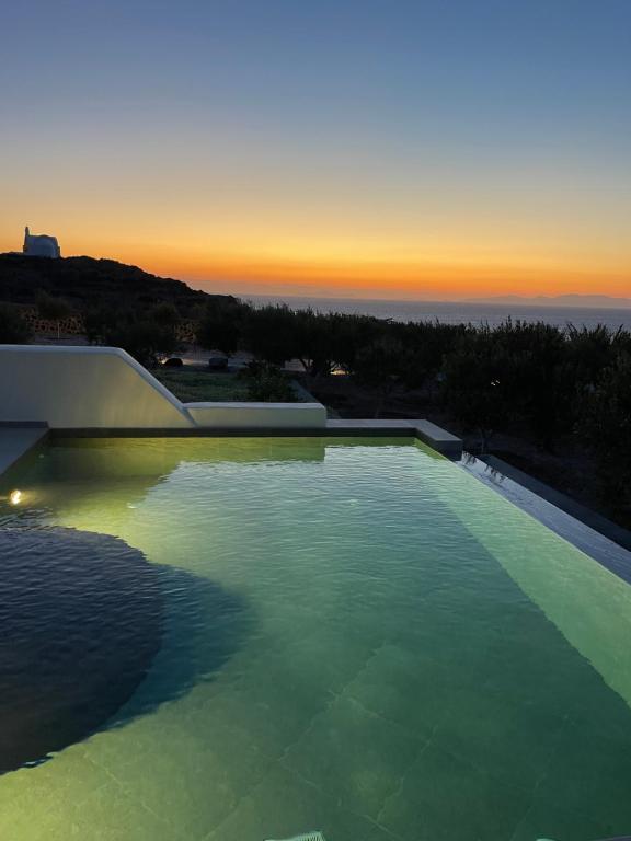 a swimming pool with a sunset in the background at Saint John Oia-The Ultimate Private Heated Pool Villas in Oia