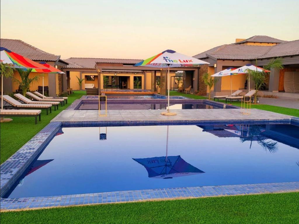 a swimming pool with chairs and umbrellas next to a house at The Lux Hotel and Resorts in Louis Trichardt