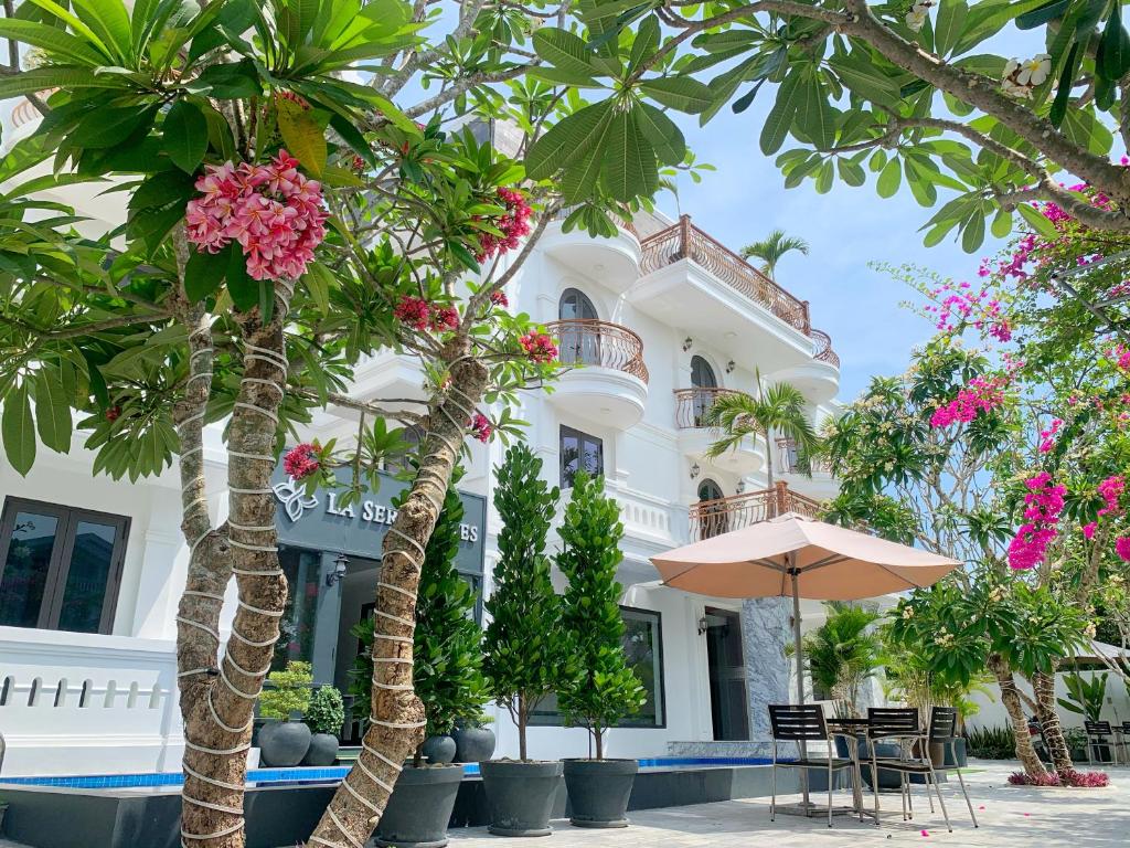 un bâtiment blanc avec des palmiers et un parasol dans l'établissement La Sera Suites Nha Trang, à Nha Trang