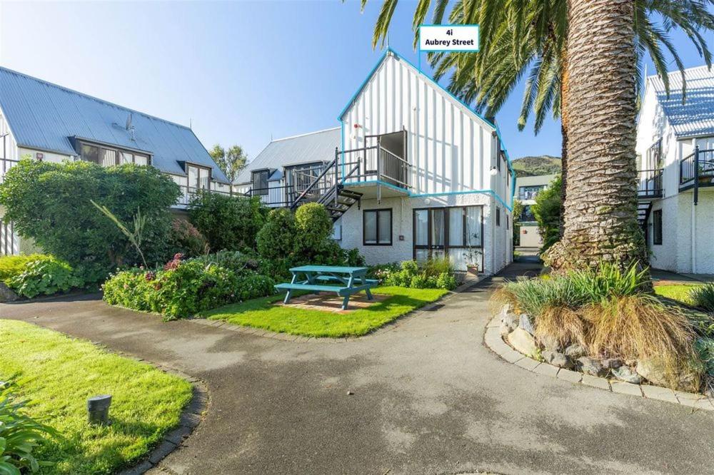 una casa con una palmera y un banco azul en Wharfside Apartment en Akaroa