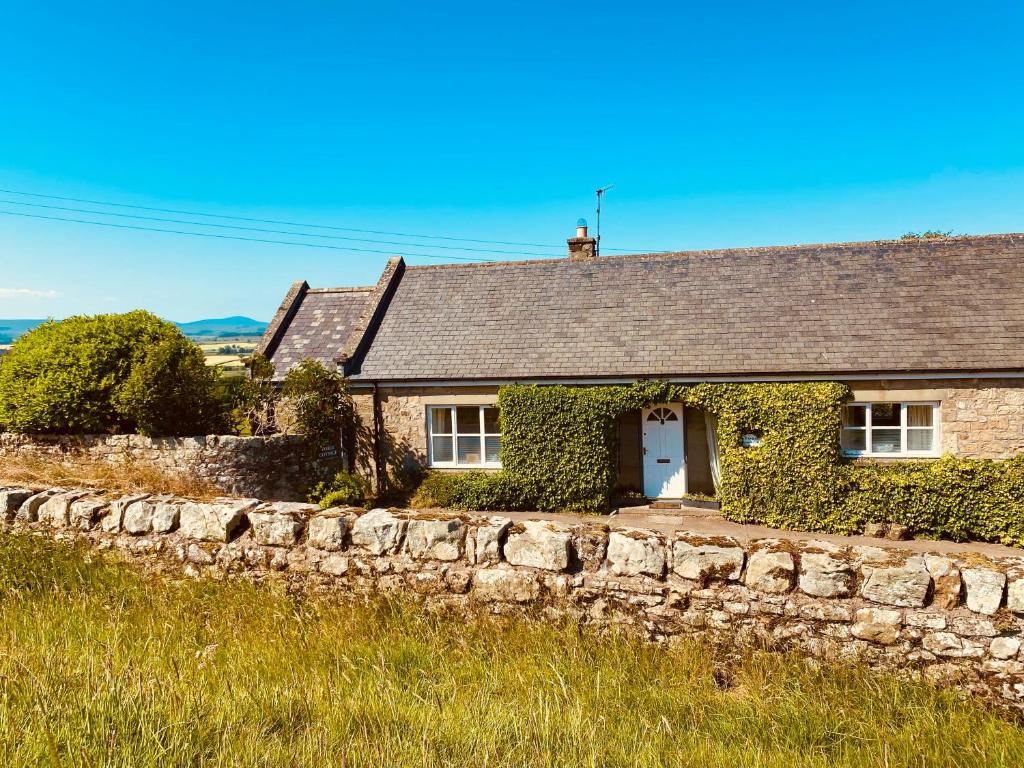 ein Steinhaus mit einer Steinmauer davor in der Unterkunft Forge Cottage in Rothbury