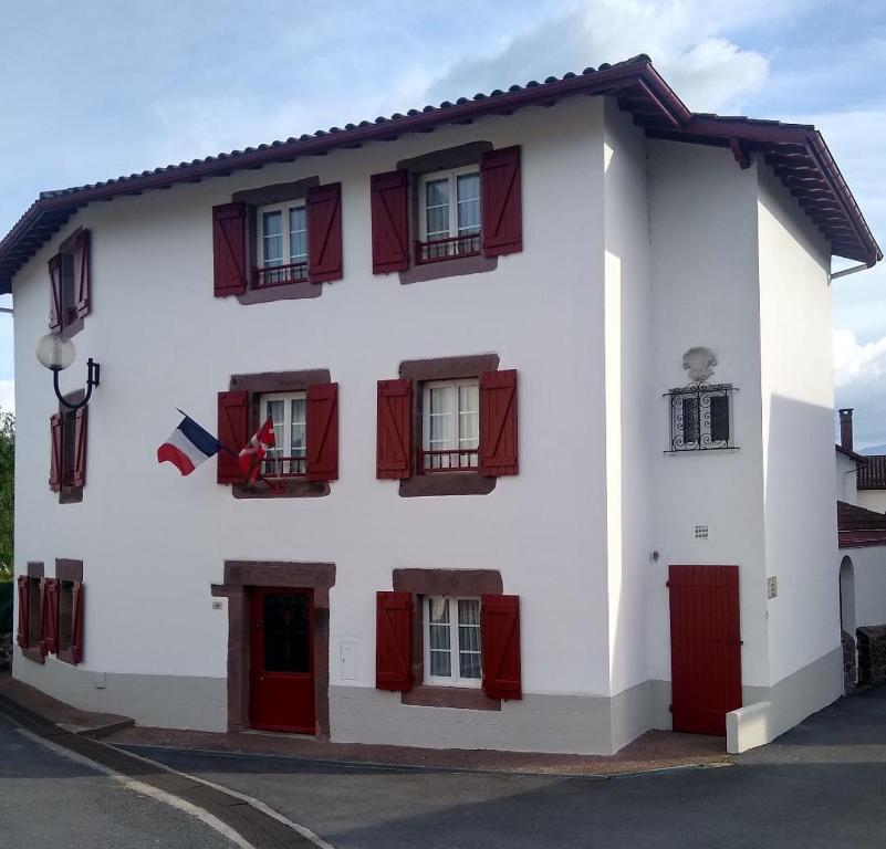 un edificio blanco con ventanas de contraventanas rojas en Maison Bidegain Berria, en Ispoure