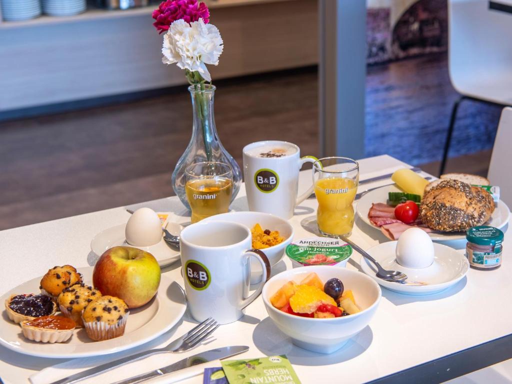 a table with breakfast foods and coffee and a vase of flowers at B&B Hotel Regensburg-City in Regensburg
