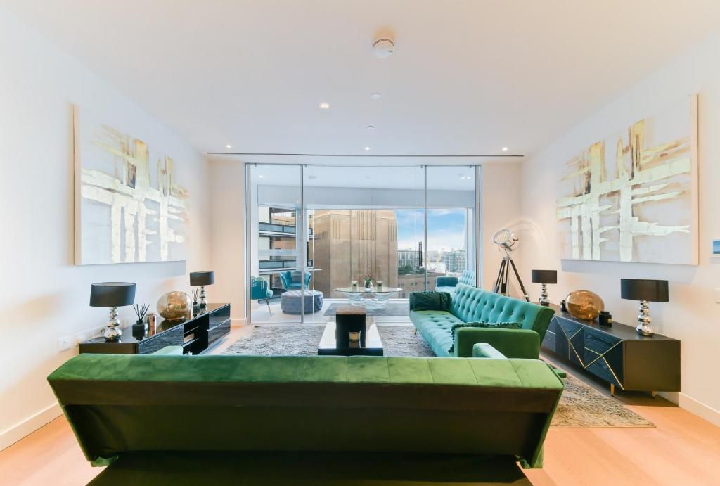 a living room with a green couch and a large window at Battersea Power Apartments in London