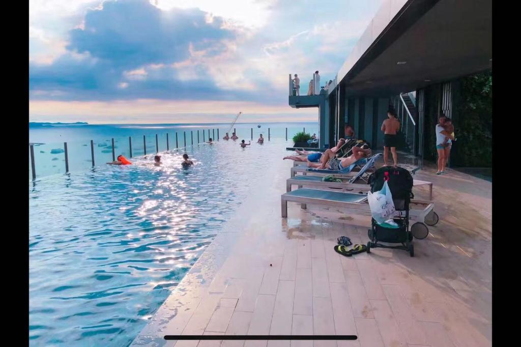 a swimming pool with people in the water at the base 网红公寓 市中心核心区顶层无边泳池俯瞰整个芭堤雅海湾 in Pattaya