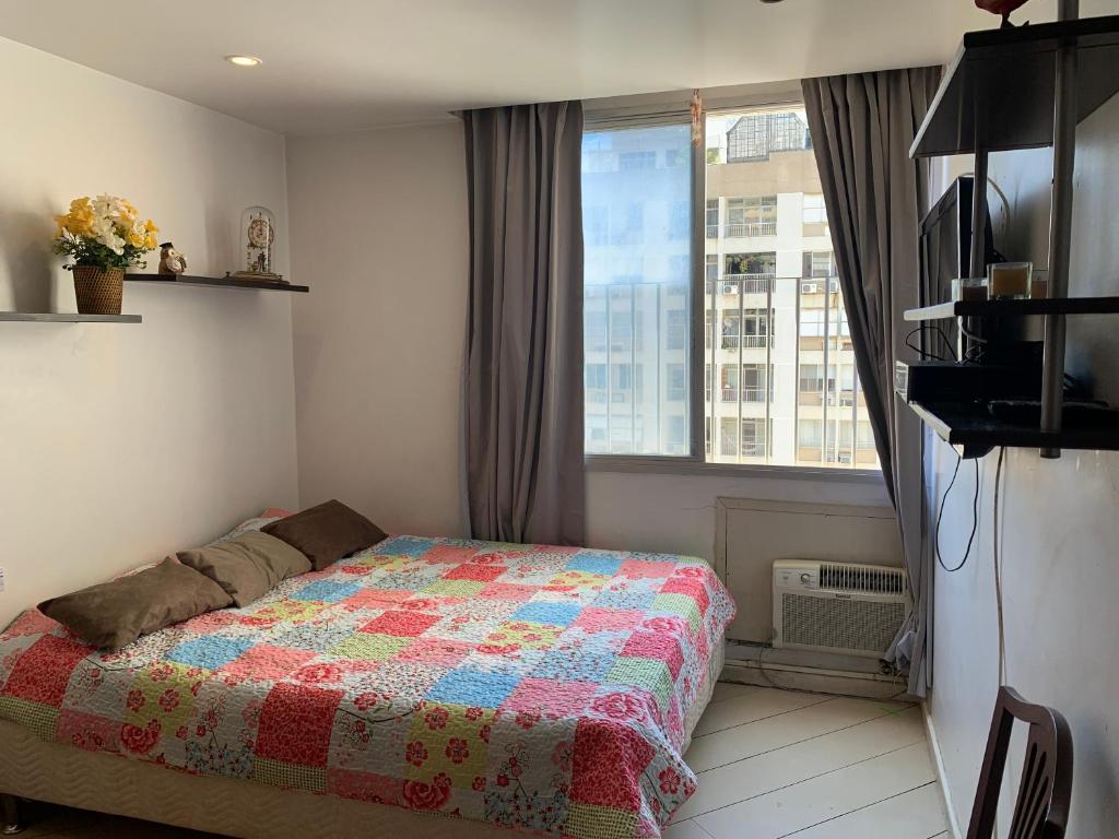 um quarto com uma cama com uma colcha e uma janela em Refúgio praiano: Apto reformado a 100m da praia no Rio de Janeiro