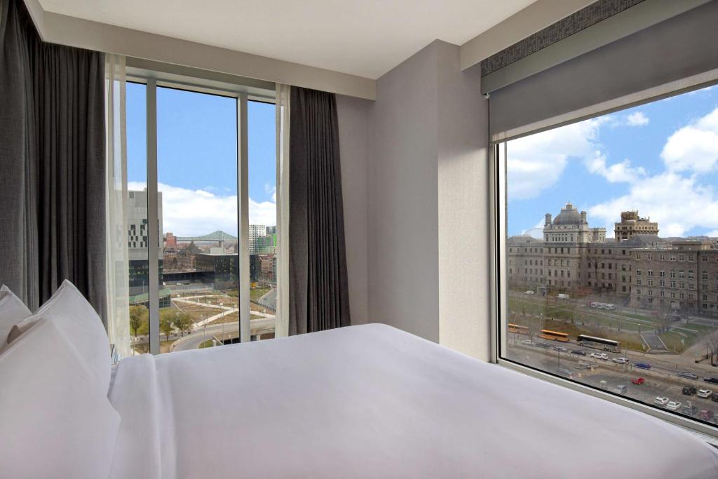 - une chambre avec un lit blanc et une grande fenêtre dans l'établissement Homewood Suites By Hilton Montreal Downtown, à Montréal