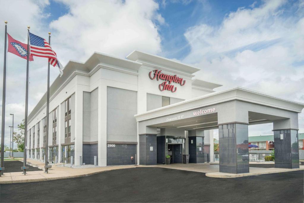 a shopping center with an american flag in front of it at Hampton Inn Jonesboro in Jonesboro