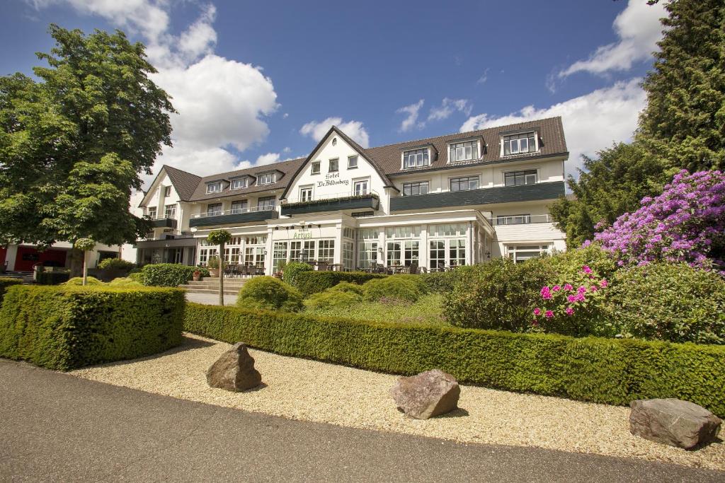 ein großes weißes Gebäude mit Büschen und Blumen in der Unterkunft Hotel De Bilderberg in Oosterbeek