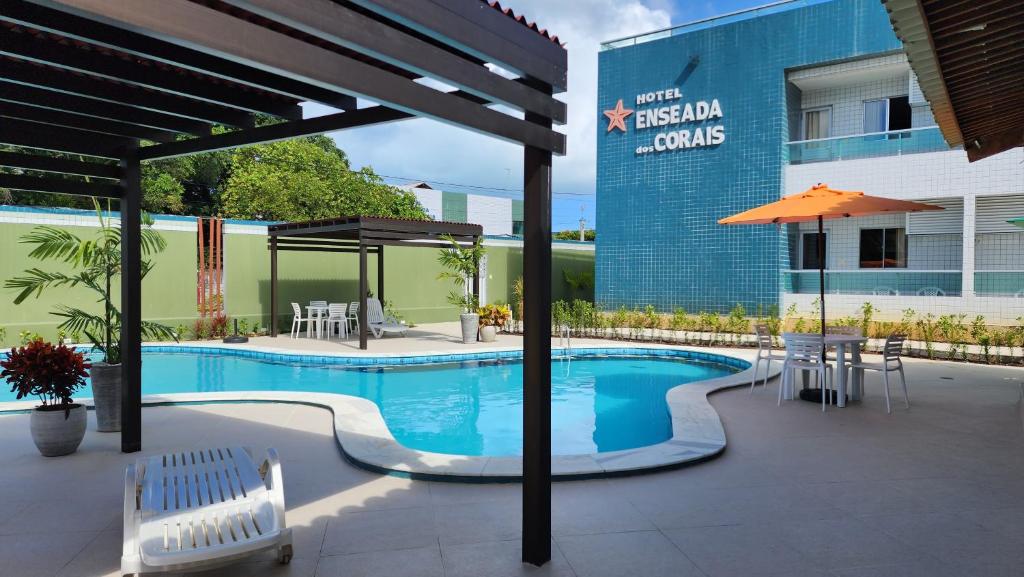 a swimming pool with tables and chairs next to a building at Hotel Enseada dos Corais in Cabo de Santo Agostinho