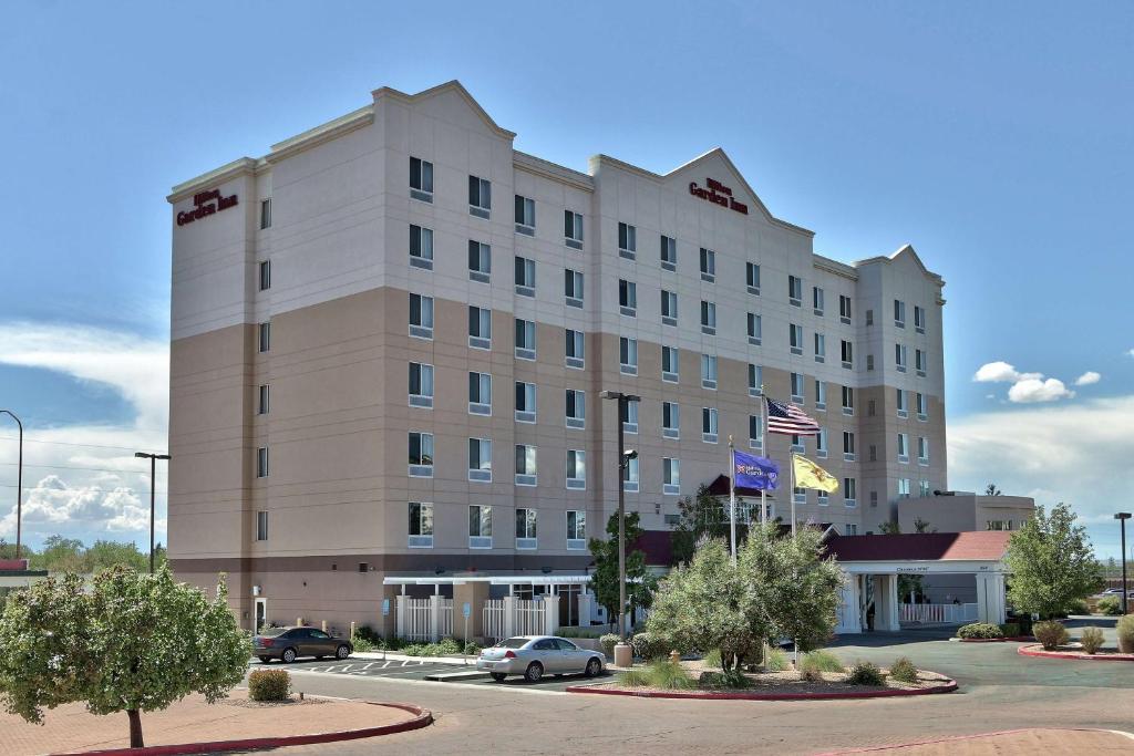 un grand bâtiment blanc avec des voitures garées dans un parking dans l'établissement Hilton Garden Inn Albuquerque Uptown, à Albuquerque