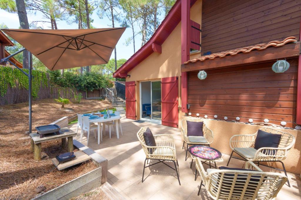 un patio avec des chaises, une table et un parasol dans l'établissement Maison pour 4 avec piscine à Lacanau, à Lacanau
