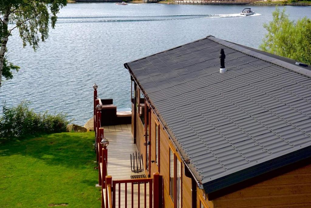 a house with a deck next to a body of water at Fable Lodge Tattershall Lakes - luxury lakeside lodge with hot tub in Tattershall