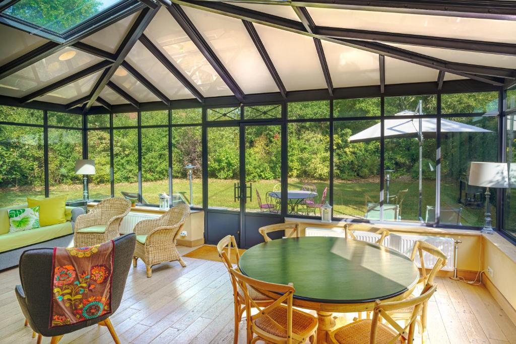 une véranda avec une table, des chaises et des fenêtres dans l'établissement Le Gîte de l'Ormoy, à Saint-Laurent