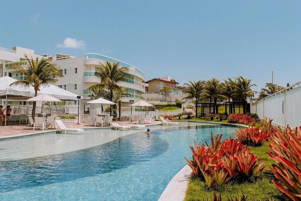 uma grande piscina com palmeiras e guarda-sóis em Qavi - Flat em Resort Beira Mar Cotovelo #InMare46 em Parnamirim