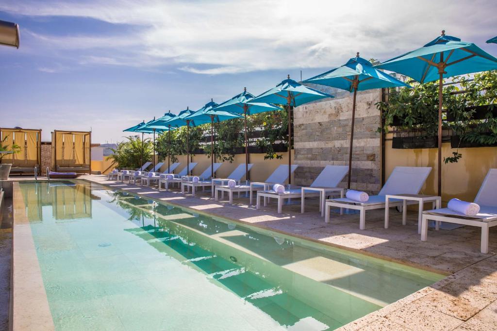 een rij blauwe parasols en stoelen naast een zwembad bij Nacar Hotel Cartagena, Curio Collection by Hilton in Cartagena