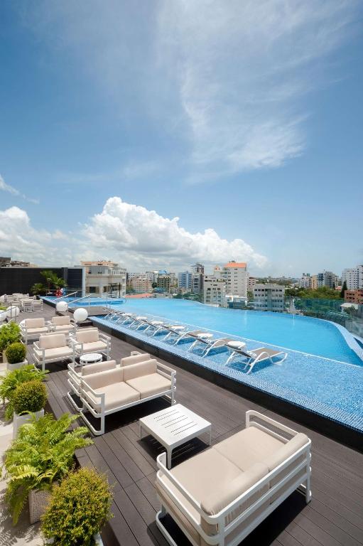 a swimming pool with chaise lounge chairs on a roof at Embassy Suites by Hilton Santo Domingo in Santo Domingo
