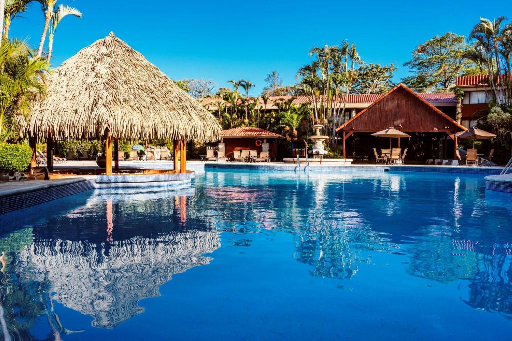 a swimming pool at a resort with a thatch roof at Hilton Cariari DoubleTree San Jose - Costa Rica in San José