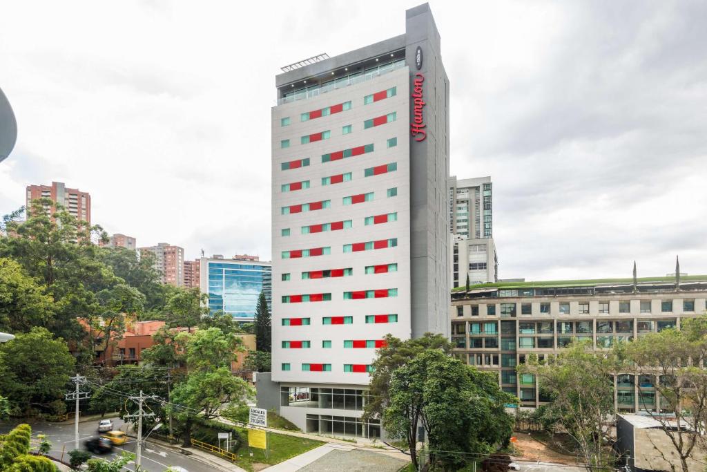 a tall white building with red windows in a city at Hampton by Hilton Medellin in Medellín