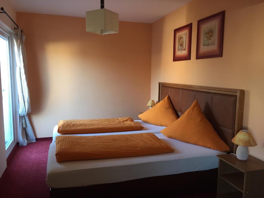 1 Schlafzimmer mit 2 Betten mit orangefarbener Bettwäsche und einem Fenster in der Unterkunft Haus der Gastlichkeit in Ratingen