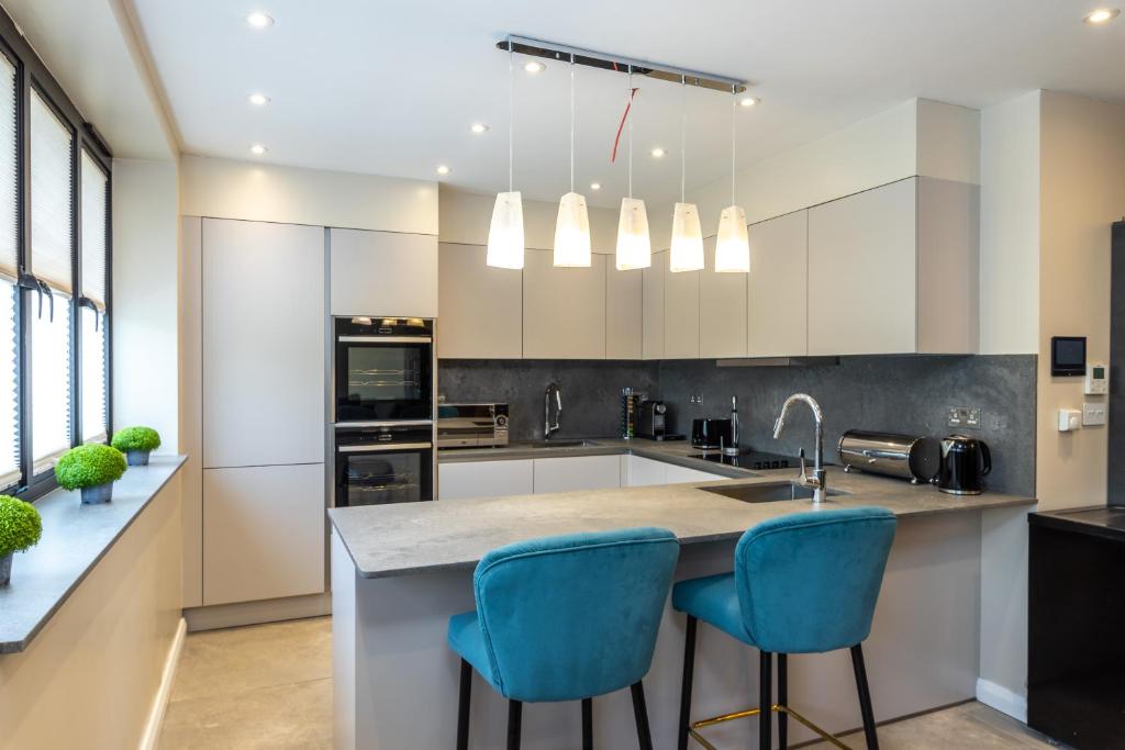 a kitchen with white cabinets and blue bar stools at Remarkable 2-Bed Apartment in London in London