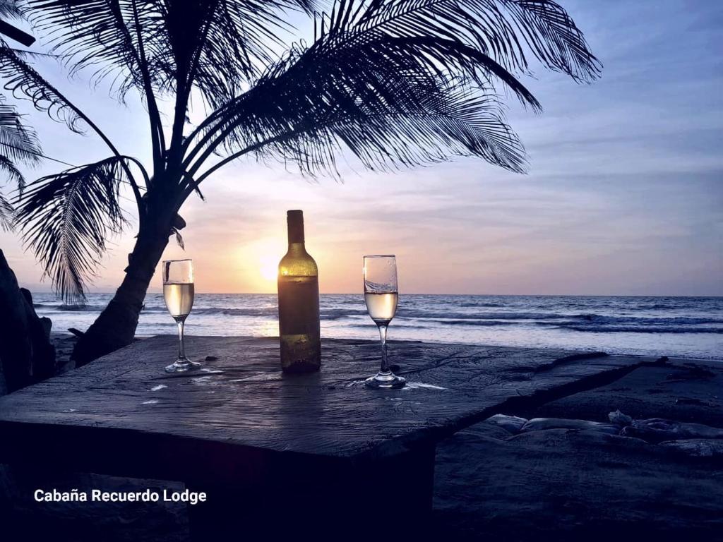 Una botella de vino y dos copas en una mesa en la playa en Cabaña RECUERDO Lodge, B & B, en Moñitos