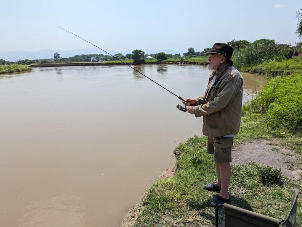 Ein Mann, der neben einem Fluss steht und eine Angelrute hält. in der Unterkunft Semliki Fishing River Camp 