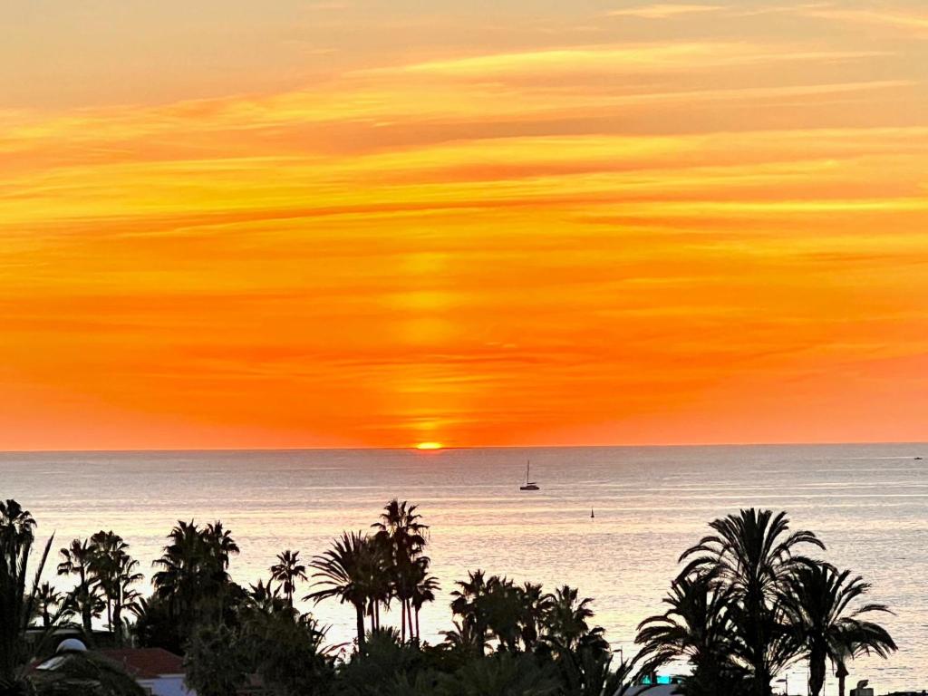 una pintura de una puesta de sol sobre el océano con palmeras en Sunset Tenerife, en Playa de las Américas