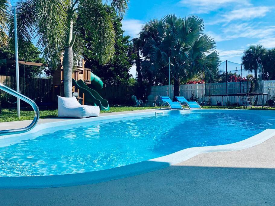 a swimming pool with a slide in a yard with palm trees at Island Vibes Beach House & 10 min walk to beach in Fort Pierce