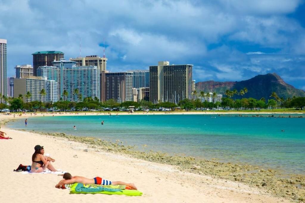two people laying on a beach with a city in the background at Amazing view from your balcony Walk to the beach 2420 in Honolulu