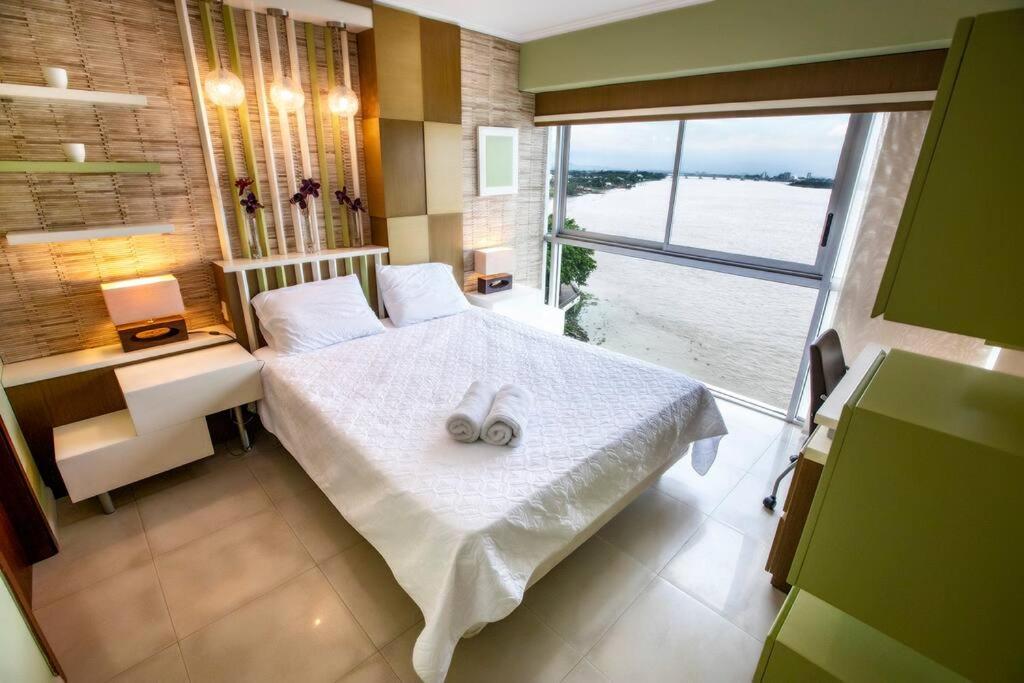 een slaapkamer met een wit bed en een groot raam bij Suit 504, vista al Rio ,con Piscina. in Guayaquil