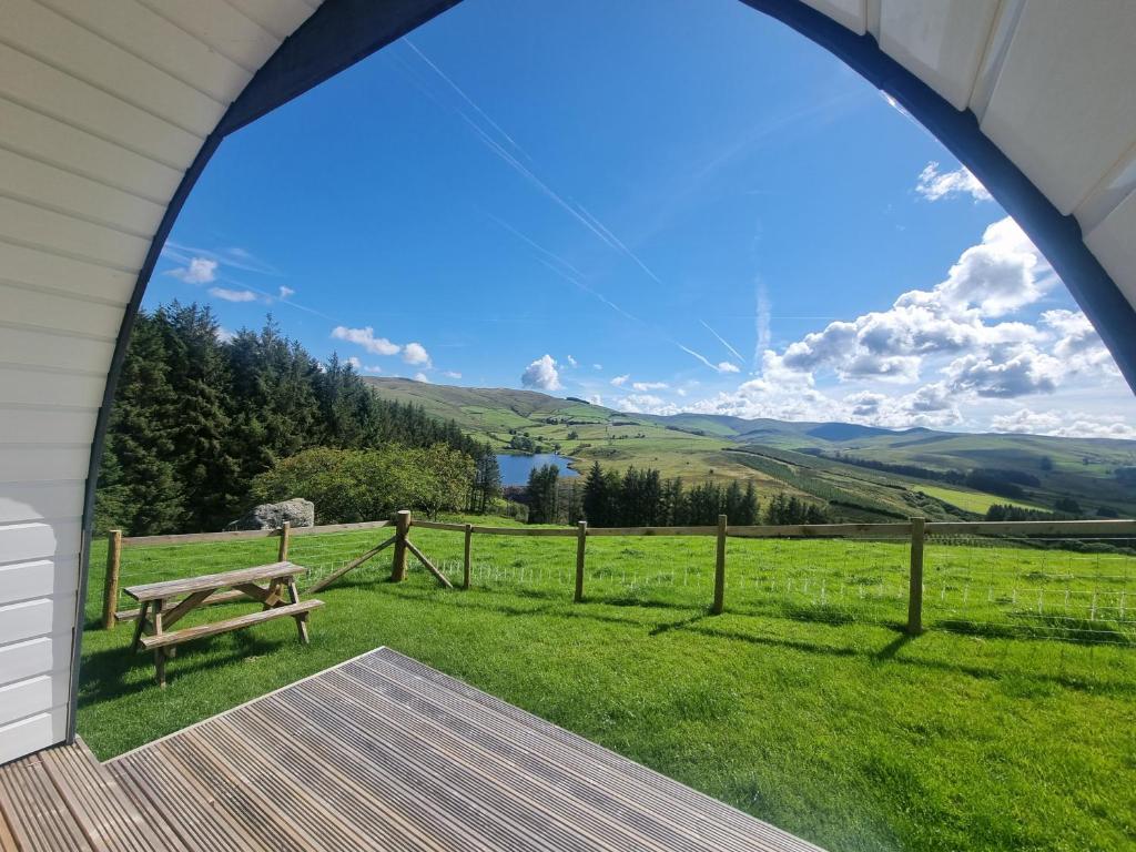 Blick auf ein Feld von einer Veranda mit einer Bank in der Unterkunft Forester's Retreat Glamping - Dinas View in Aberystwyth